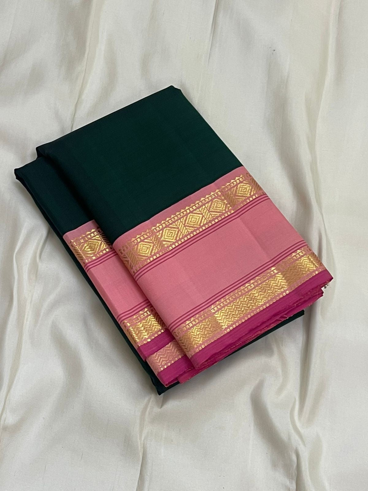Folded Adar pachai green Kanchipuram silk saree with thamarai pink rettapet gold zari border on ivory background