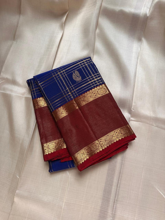 Sapphire Ruby Kattam – Pure Kanchipuram Silk Saree
sapphire blue body with gold kattam checks & buttas
Contrast ruby-red korvai borders with intricate gold zari weave
Grand ruby-red pallu with floral motifs
Silk Mark Certified | ships in 2 weeks