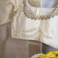 Close-up of a white blouse with gold embroidery on a hanger, with flowers in the foreground.