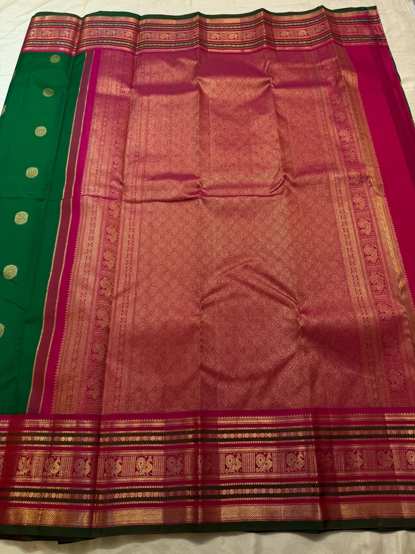 Wide magenta Varisaipet border with dense gold zari bands and Kili Yazhi motif panels on emerald Kanchipuram silk