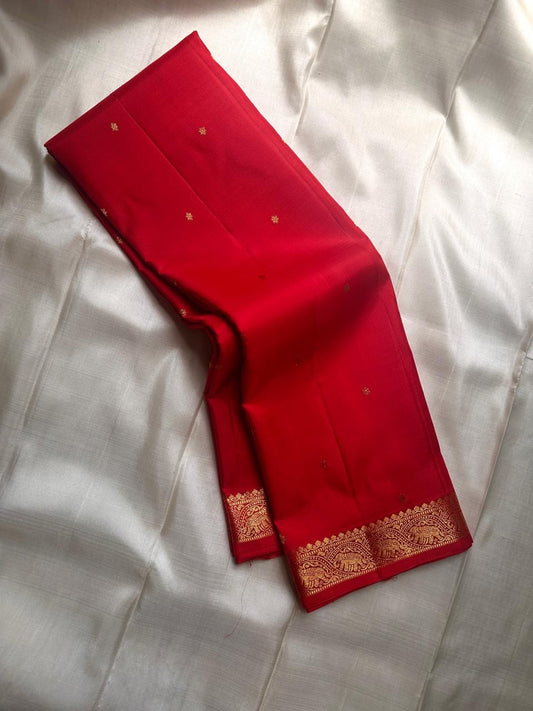Mahima –red
A luminous red pure silk Kanchipuram drape adorned with delicate baby  kamalam buttas. The petite border features muthu seer and zari-woven elephants with floral vines. Its grand pallu showcases annams, golden grids, and Rudhraksham seer.