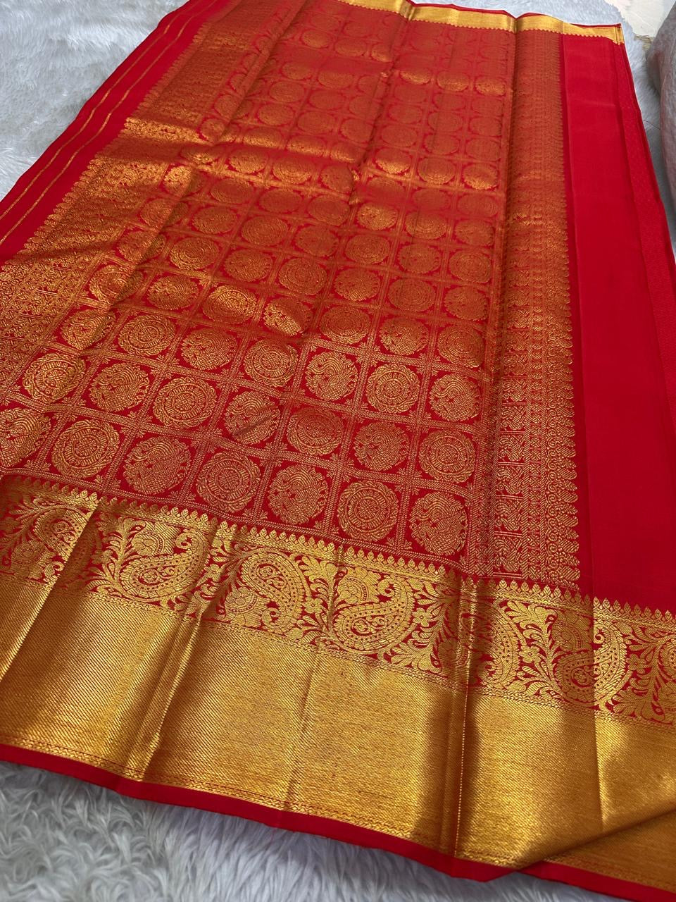 A traditional Kanjivaram (Kanchipuram) silk saree, vibrant red orange peacock floral motifs bavanji border and ornate grid motif Pallu