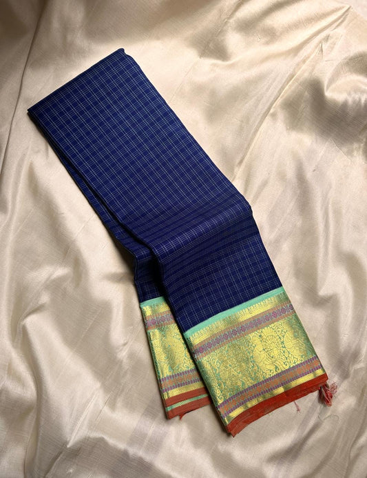 A striking blend of tradition and bold design, this navy blue Kanchipuram silk saree features delicate grid-like checks across the body. What sets it apart is the vibrant mint green and gold zari border, intricately woven with paisley and floral motifs