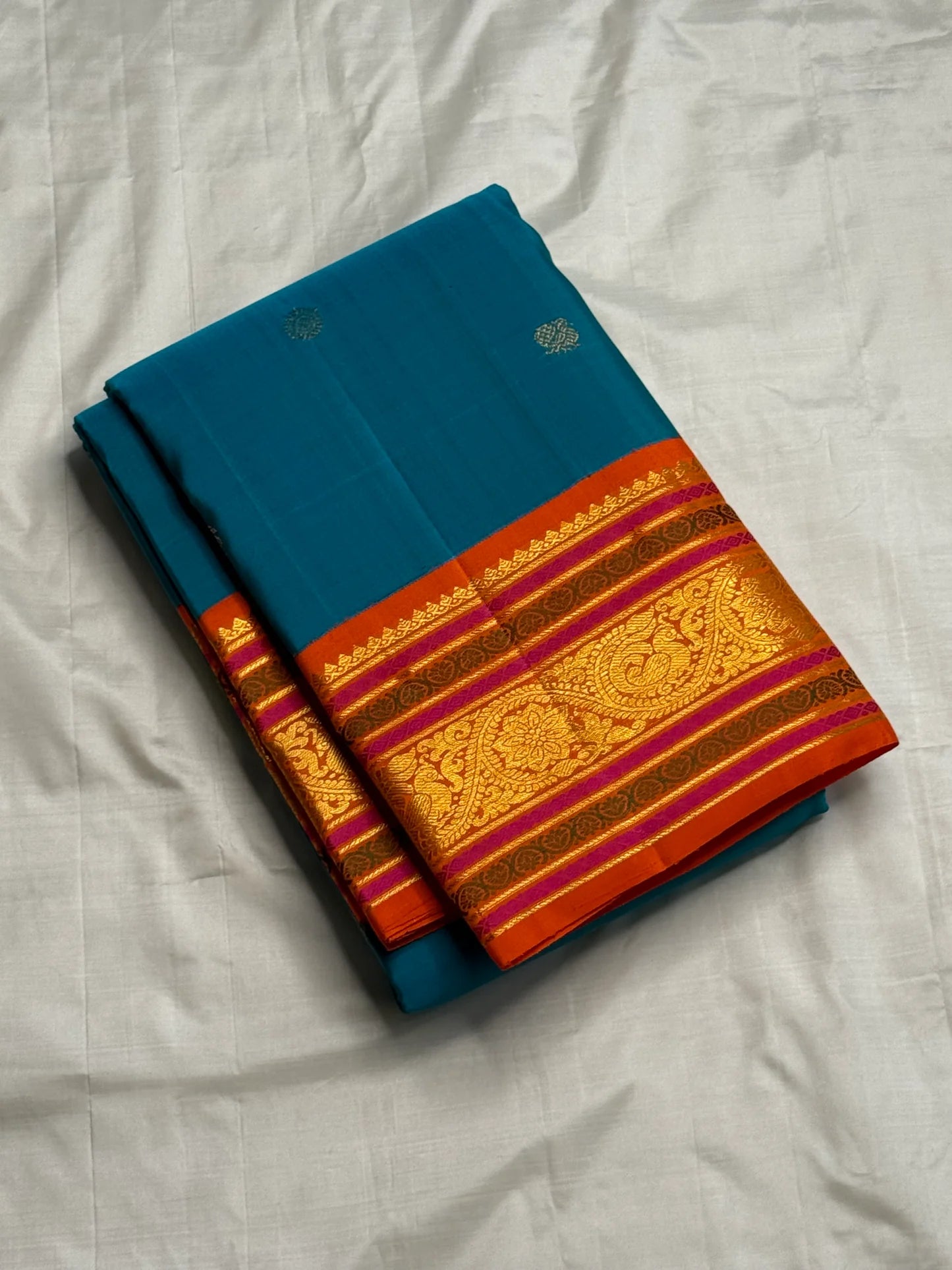 Aazhi Teal — Pure Kanchipuram Silk Saree
Teal body with silver-zari rosette buttas and korvai kavi–magenta borders in gold-zari brocade.
Silk Mark Certified • Free Shipping within USA • Ships in Two Weeks ✅