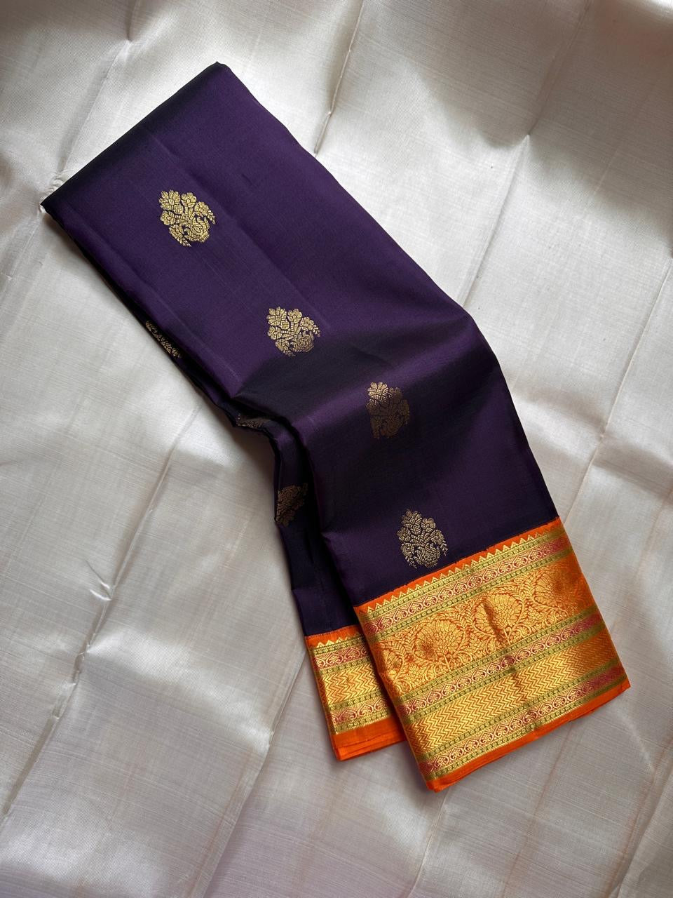 Jamun Purple Kesar – Korvai Kanchipuram Pure Silk Saree

Regal jamun-purple body adorned with antique-gold floral buttas

Kesari-orange korvai border with chakra roundels, vines & chevron zari

Free shipping withinUSA silk mark certified ships in 2 weeks