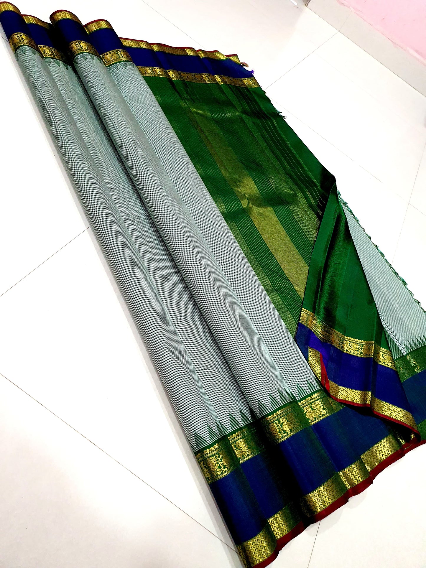 Podi Kattam Emerald Pillar Moggu – Pure Kanchipuram Silk Saree
Seafoam–Ice Blue Micro Checks with Korvai Emerald Green Border
Neelam Blue Panel & Gold Zari pillayar Moggu Motifs
Rich Emerald Zari-Striped Pallu | silk mark certified Saree ships in two week