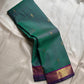Varnam is a pure Kanchipuram silk saree in rich emerald green with subtle dual-tone shading. Woven gold zari buttas dot the body, while a petite purple border woven with intricate zari adds refined contrast. Arai maadam Pallu, jewel toned classic !
