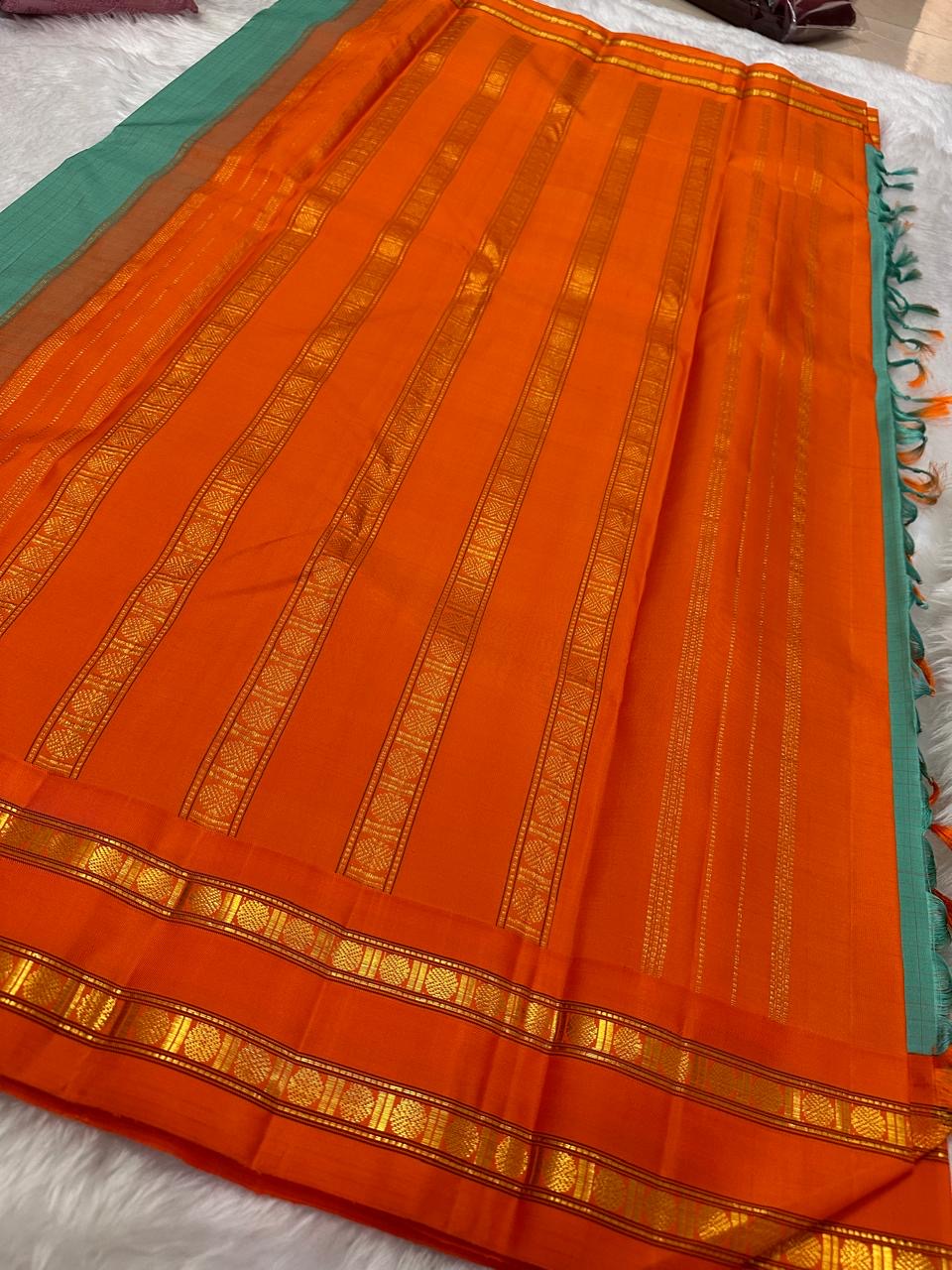 Sharvani blue sea green – sea green  Checked Silk Saree with an Orange red  shot color Zari Border & Vibrant Pallu A timeless silk saree featuring a cream body with delicate red checks, complemented by a striking churan orange  zari border pallu.