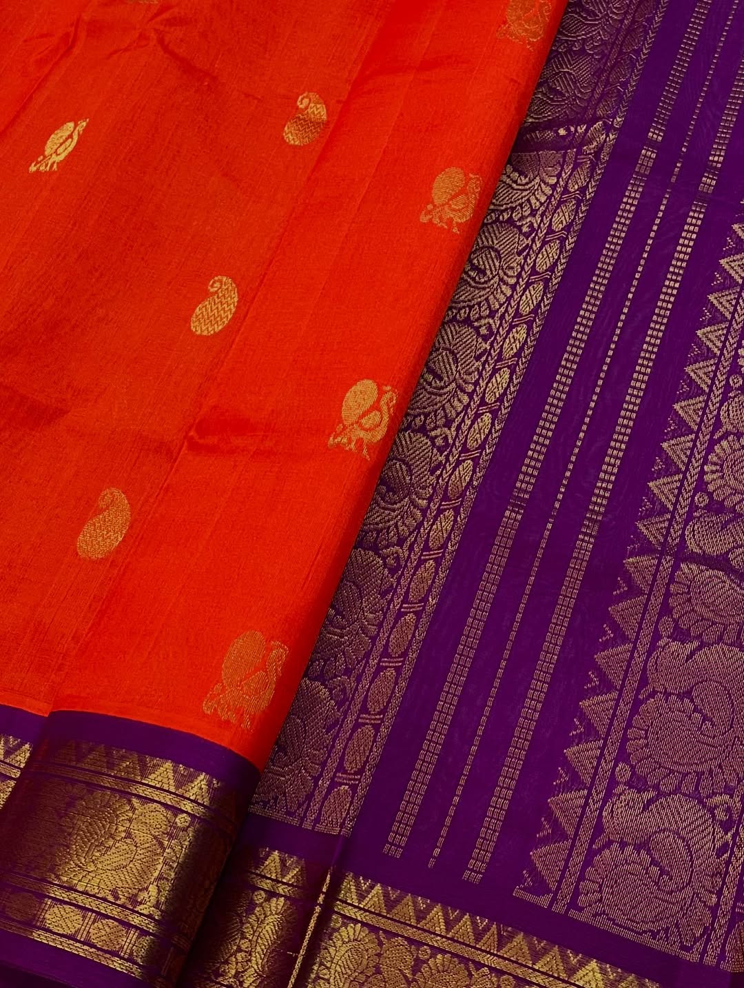 An exquisite blend of tradition and vibrancy, this silk cotton saree features a radiant orange body adorned with elegant gold zari buttas, The rich contrast border and pallu in royal purple and intricately woven with traditional gold zari motif