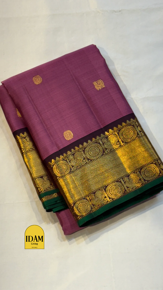 Tanaya features a regal mulberry mauve purple body adorned with golden kamalam and mayil buttas. Its elegant dual-tone border—coffee brown on top and emerald green below with rich temple-inspired zari work with medallions and florals woven, rich Pallu.