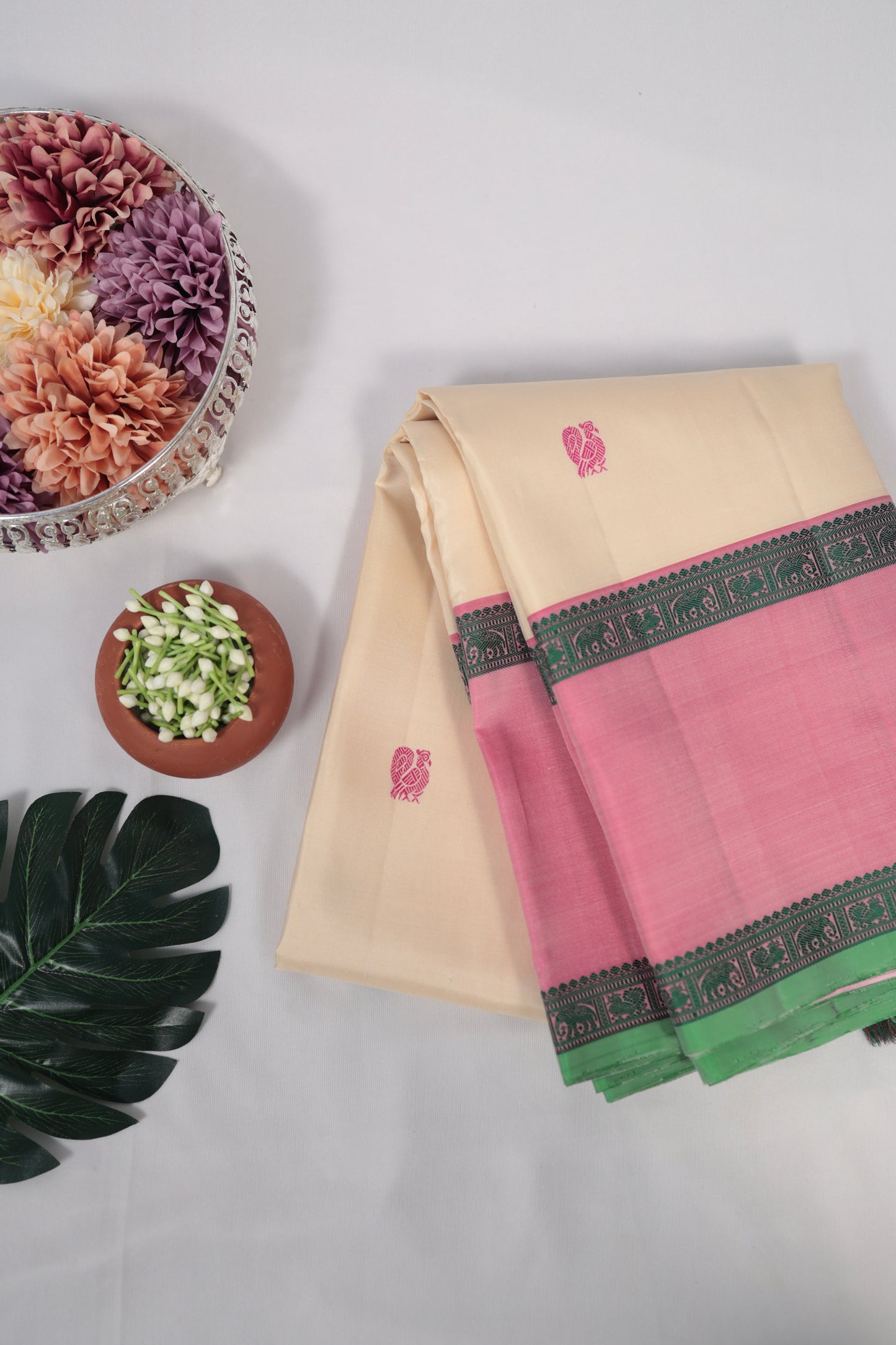 Ivory and lotus pink no-zari Kanchipuram silk saree draped over a chair, showing contrast pallu and tassels on a white background