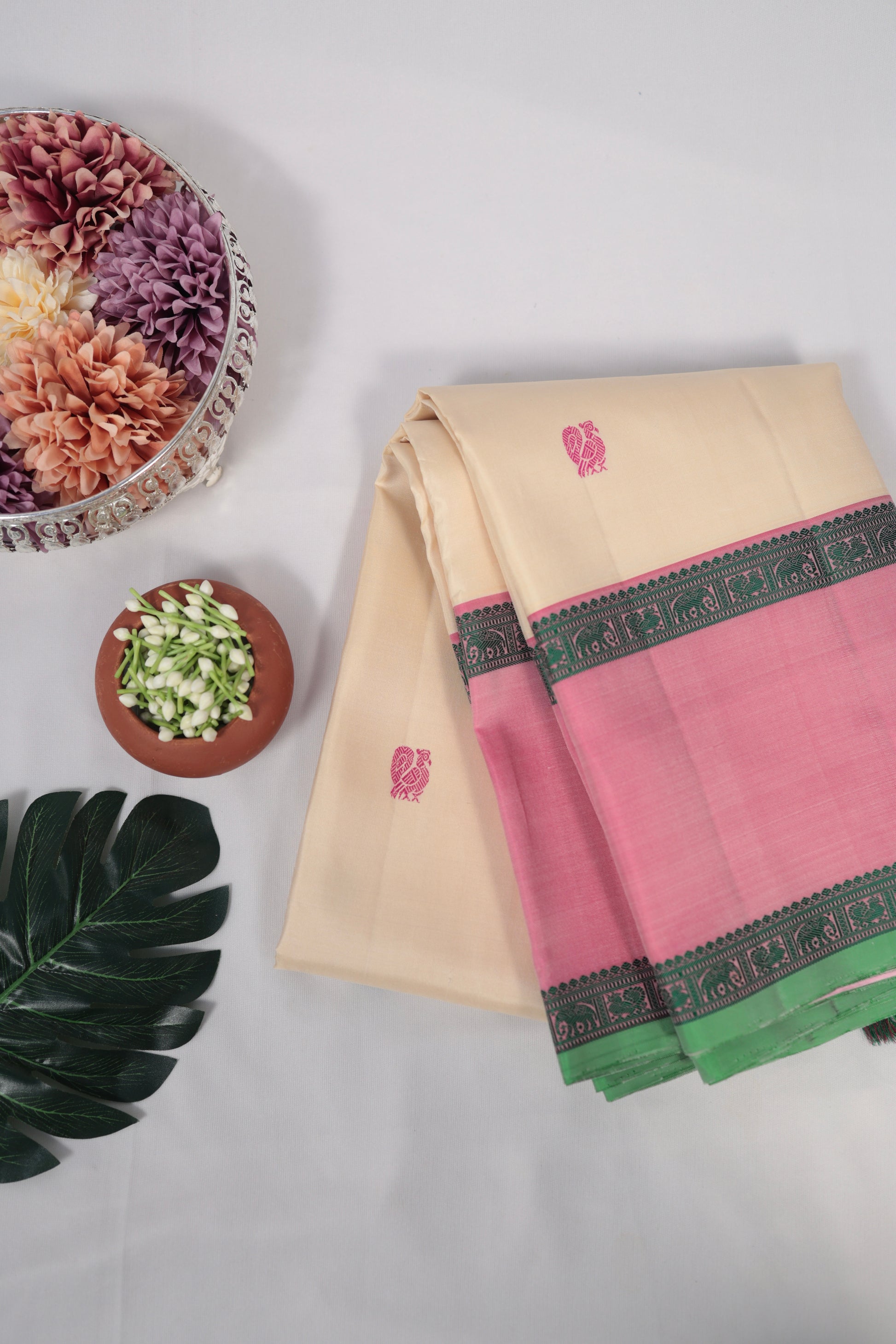 Ivory and lotus pink no-zari Kanchipuram silk saree draped over a chair, showing contrast pallu and tassels on a white background