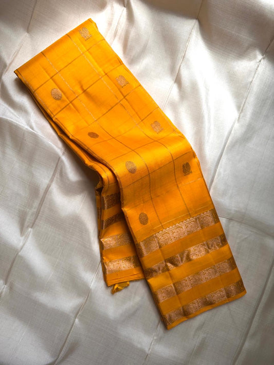 Kanaka – Sunlit Mustard Kanchipuram Silk Saree with Checked Zari Buttas and Gold Striped Border
A radiant weave that captures the warmth of tradition and the glow of celebration