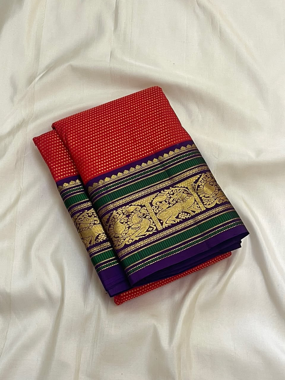 Full folded view of Kancheepuram Butta saree showing dense red gold butta body and purple-green border