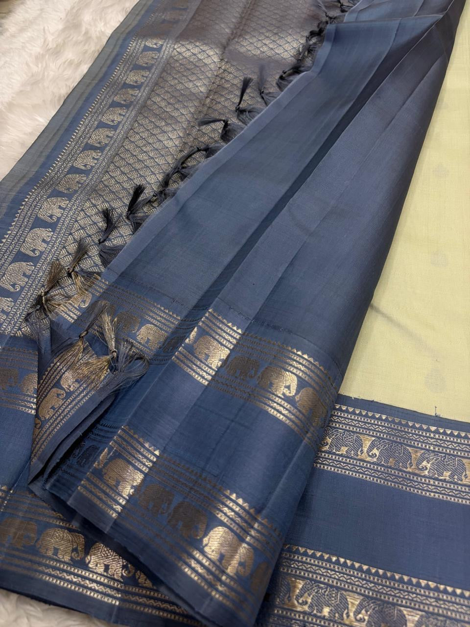 Folded view of the handwoven pale gold and steel blue Kancheepuram pure silk saree showing Teardrop Butta body and Rettapet Yaanai border