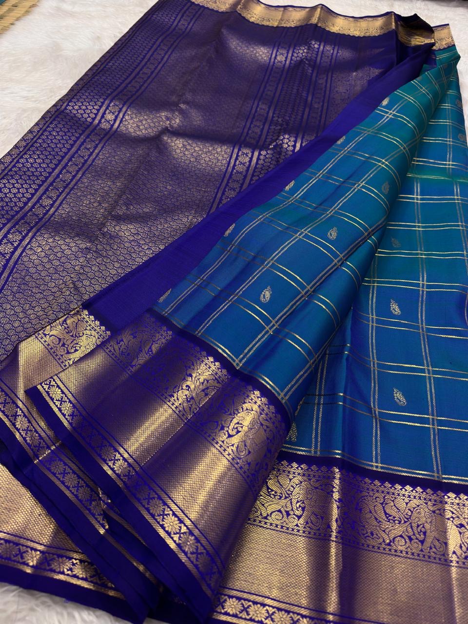 Close-up of shot colour peacock blue-green silk body with Zari Kattam grid and Yaanai elephant and Maanga mango buttas in antique gold zari — handwoven Kancheepuram silk