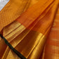 Handwoven Kanchipuram Veldhari saree in shot amber golden orange with green selvedge, Zari Kattam grid, and Maanga Butta, full folded view