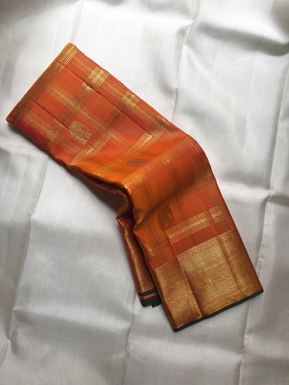 Full folded view of Kanchipuram Veldhari saree showing shot amber golden orange body and green selvedge