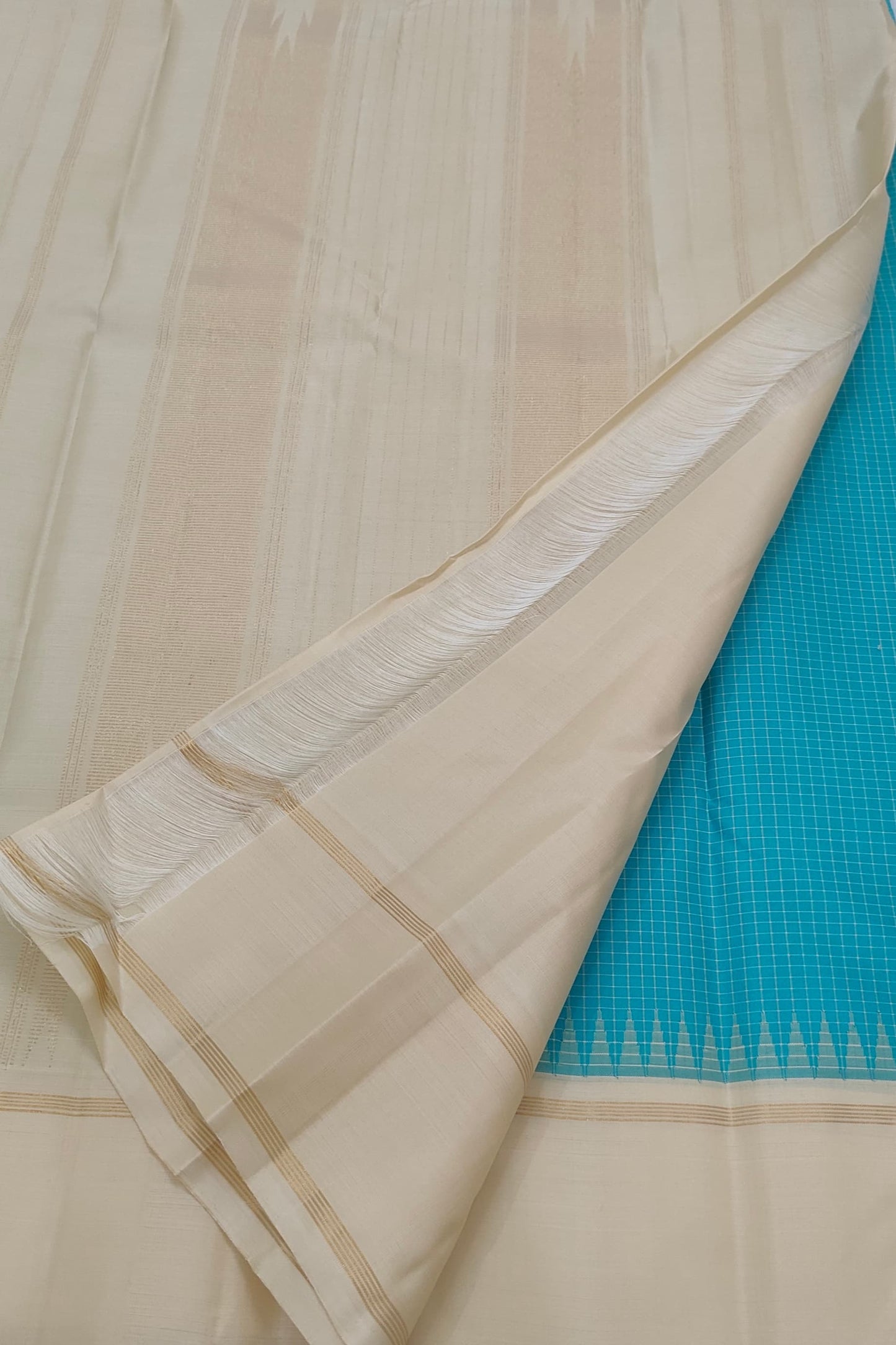Folded view of the handwoven peacock blue Kanjipuram silk saree showing Kanchi Kattam body and ivory Pillayar Reku border