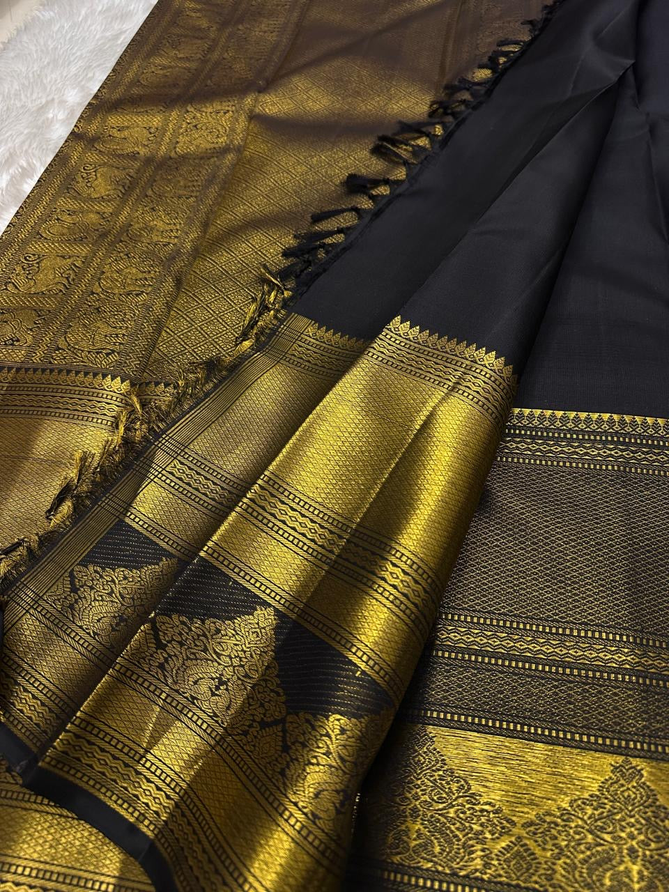 Pure Kanchipuram silk saree drape view with black body, vertical gold zari stripes, and wide gold zari border near tassels