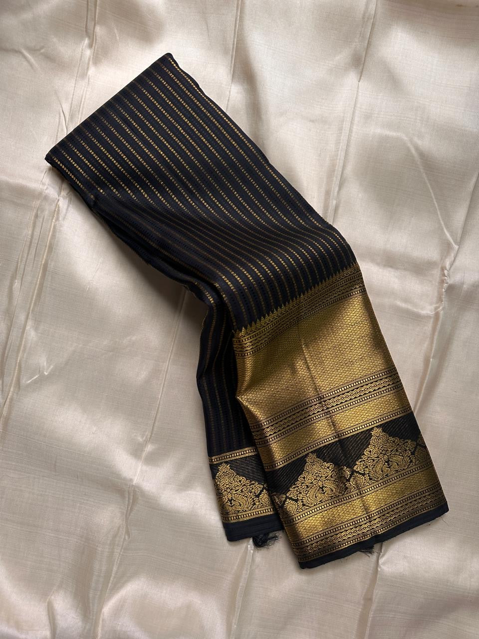 Pure Kanchipuram silk saree folded showing wide gold zari border with black edge and gold woven motif band