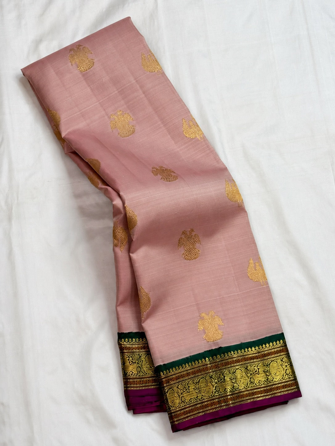 Folded view of petal pink Kanchipuram silk saree with contrast emerald green zari border and magenta edge