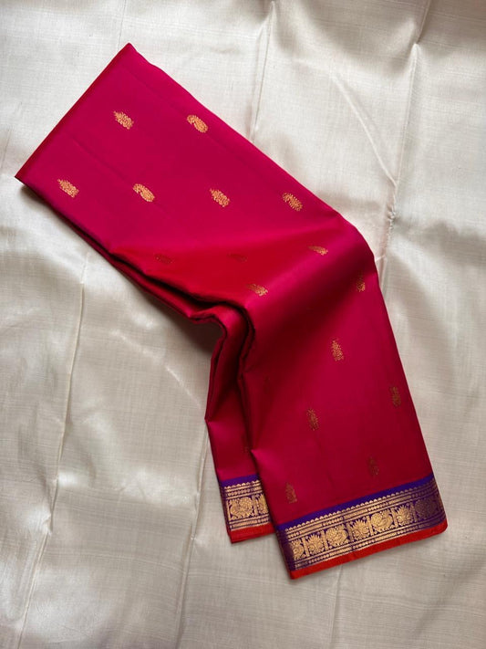 Rani pink Pure Kanchipuram silk saree shown draped with scattered gold zari buttas and blue zari woven border.