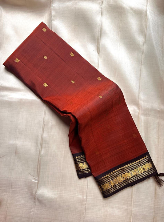 Draped view of rust Pure Kanchipuram silk saree with scattered gold zari buttas and a black zari woven elephant border.