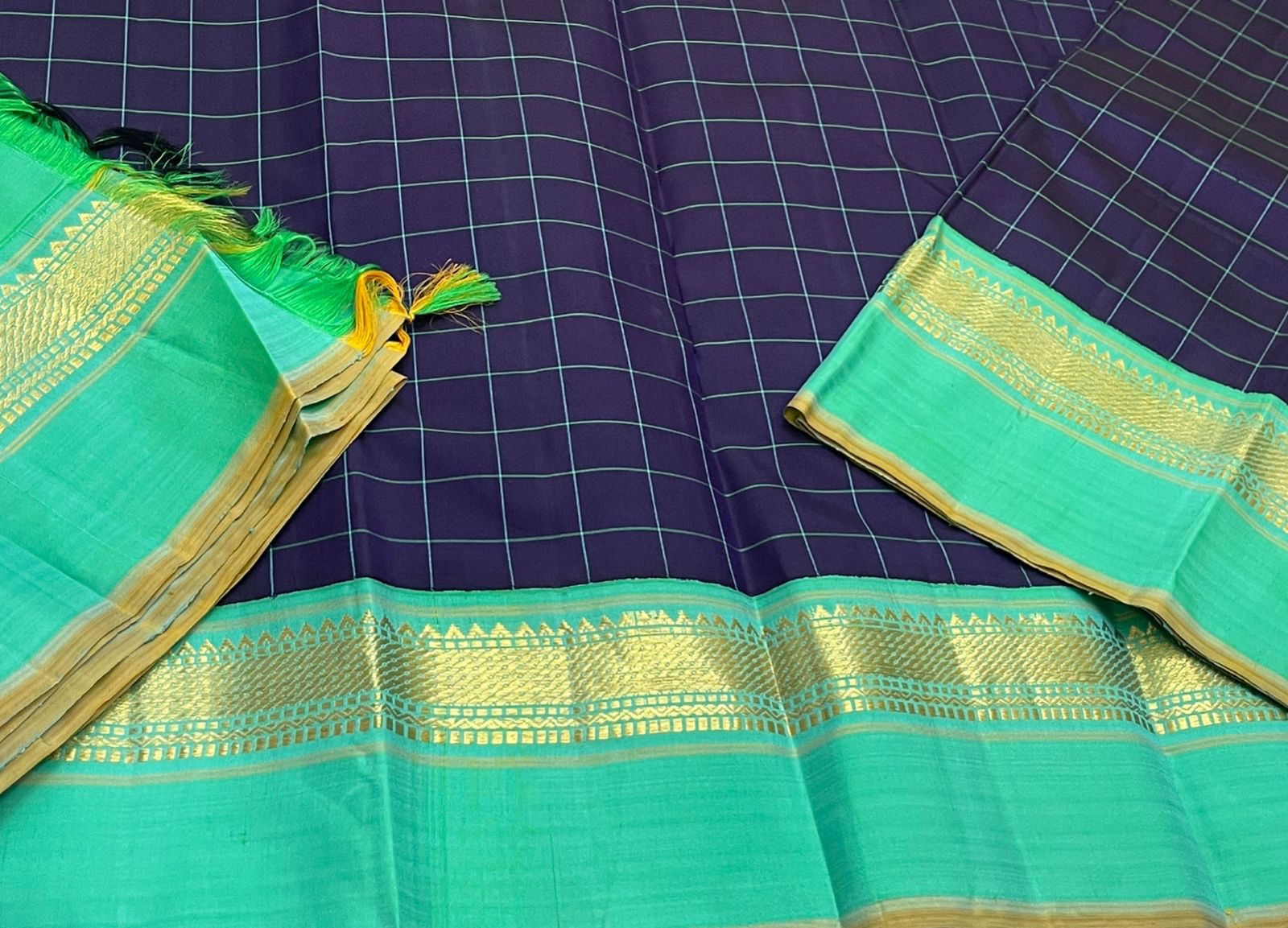Closeup of sea green Pure Kanchipuram silk saree border with gold zari woven bands and tassels beside navy checked body
