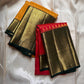 Two folded sarees shown together, one in mustard and one in red, each with a wide gold zari woven border and green edging.