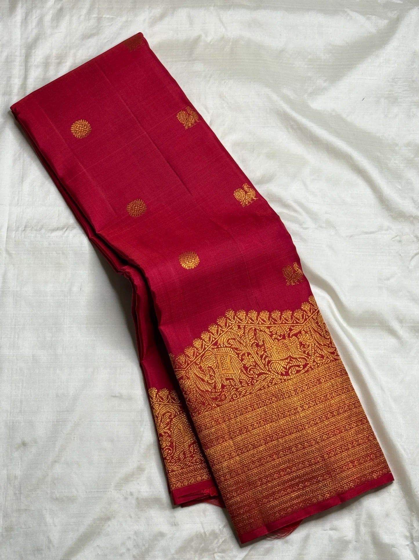 Folded Red Deep Pink Kanchipuram Butta saree showing antique-gold figurative Turning Border and fine zari registers.