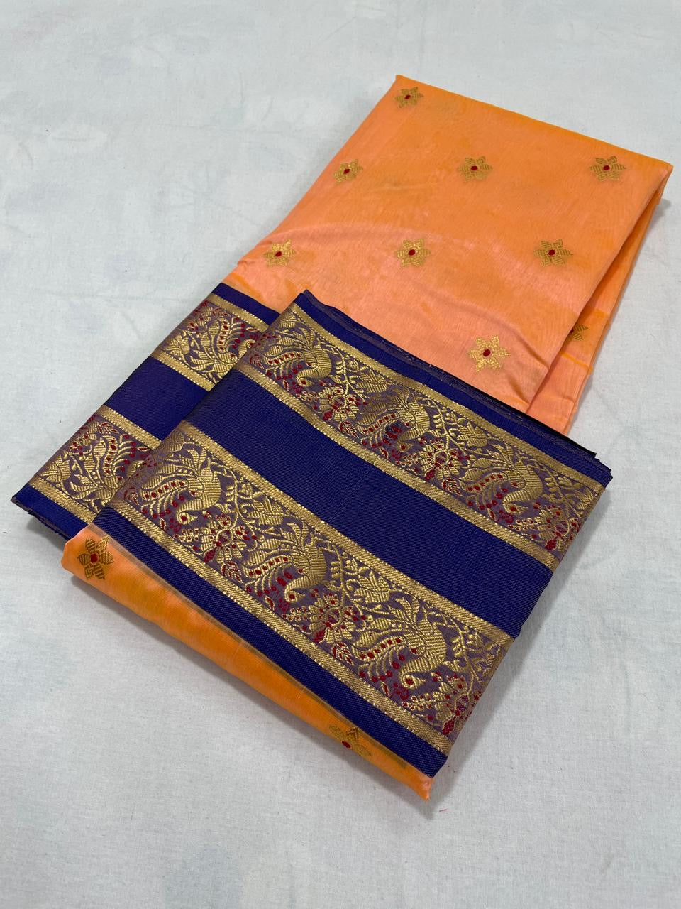 Folded Apricot Peach Chanderi silk saree with gold floral buttas and Royal Blue woven border