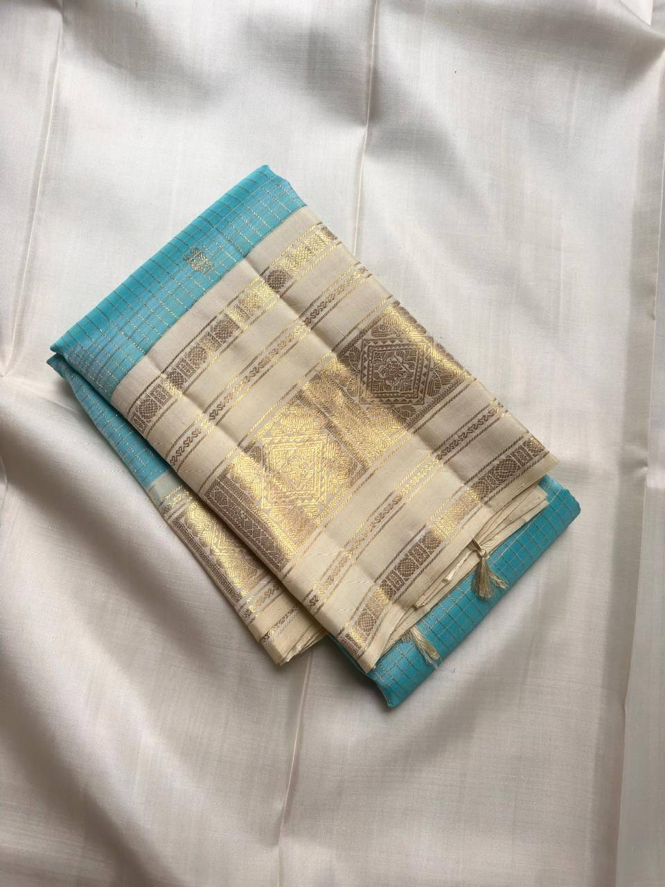 Folded Aqua Blue and Warm Ivory Zari Kattam saree showing intricate gold and silver-toned metallic weaving.