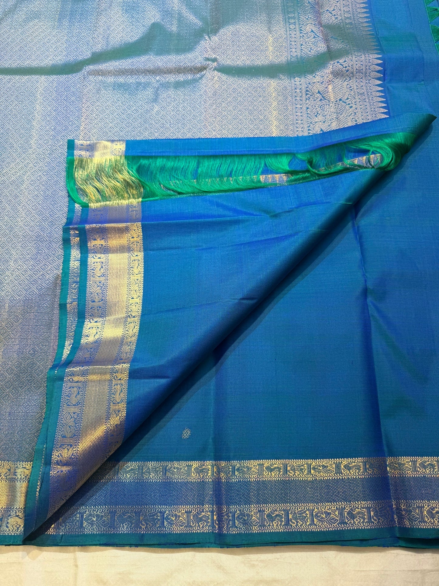 Close-up of scattered zari buttas on a peacock blue KanchiPattu silk saree body