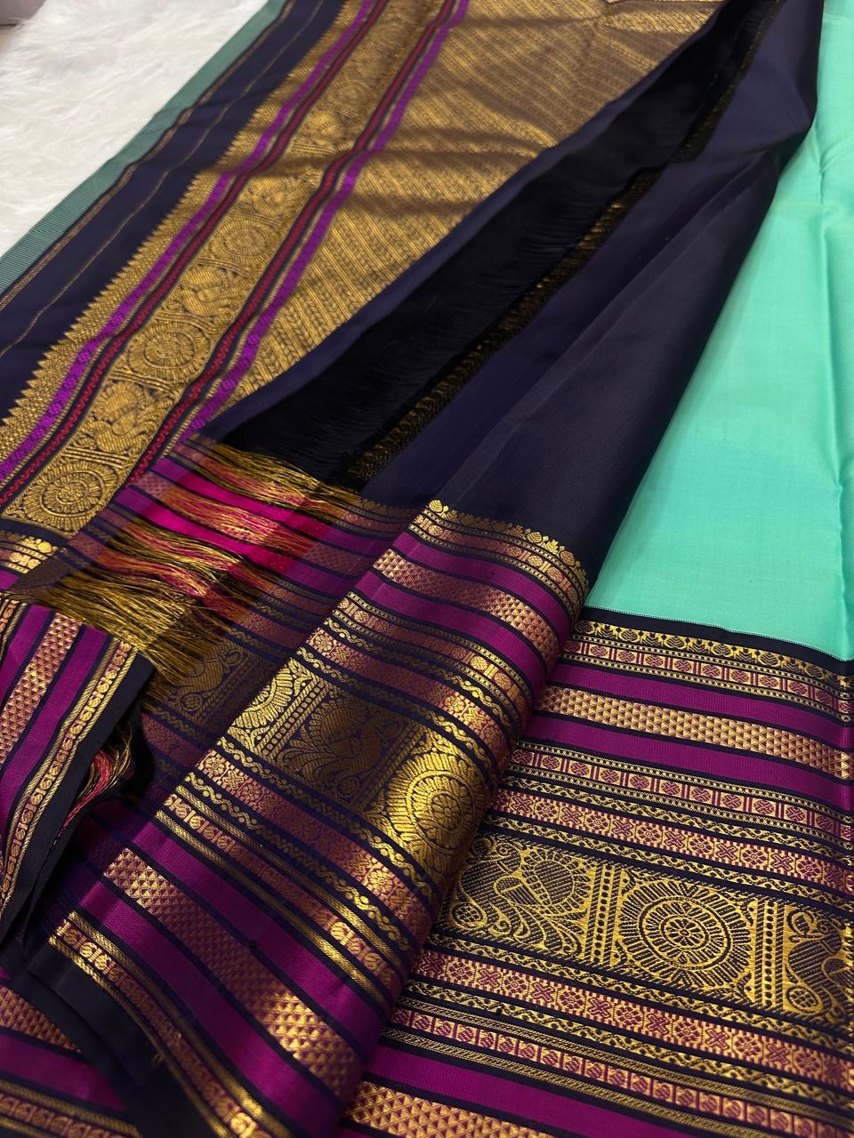 Folded turquoise Kanjipuram saree showing elaborate navy Vadamalli and gold peacock border.