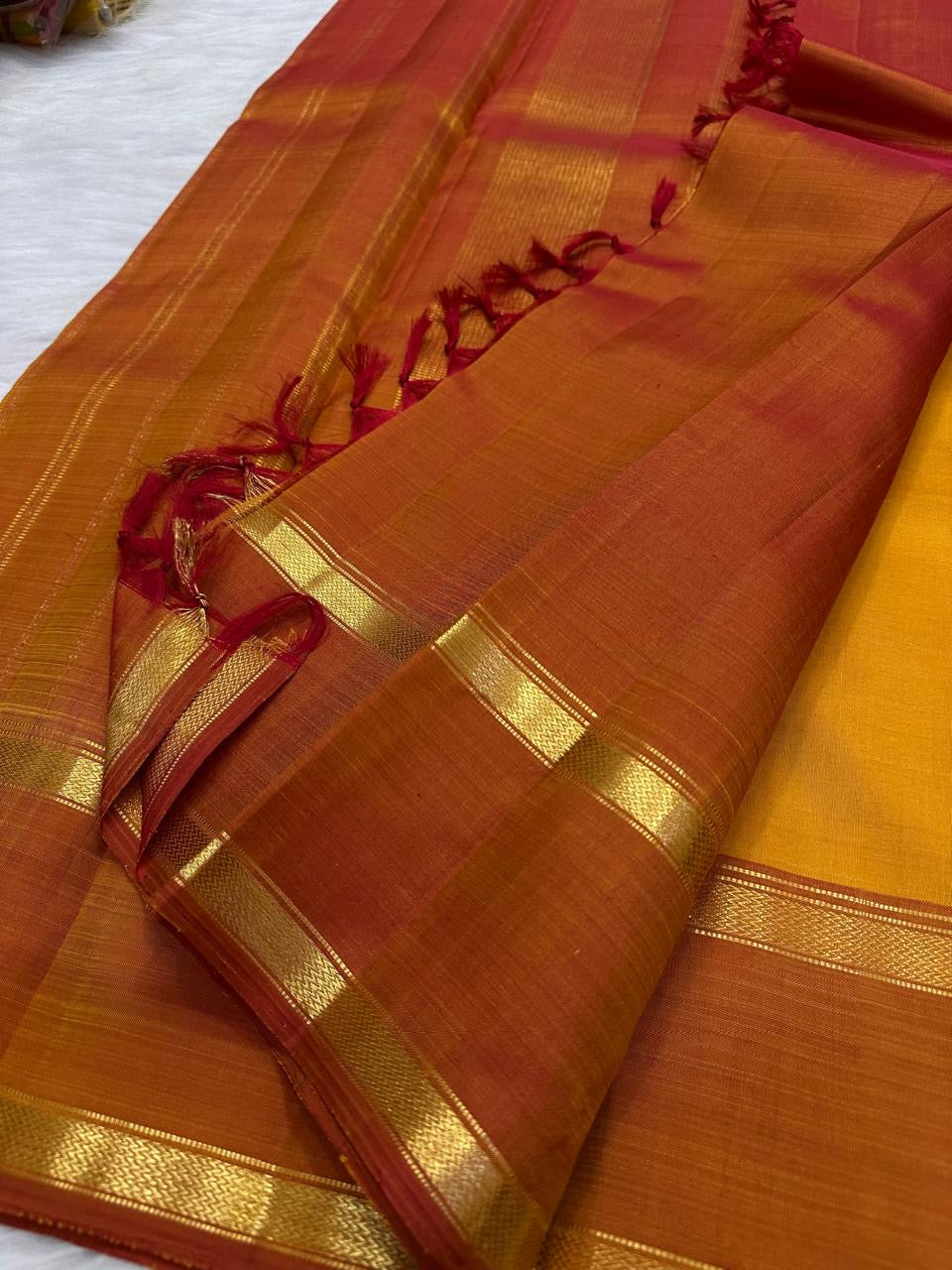 Gold zari band detail on Arakku red border, Manjal orange Kanjeevaram saree