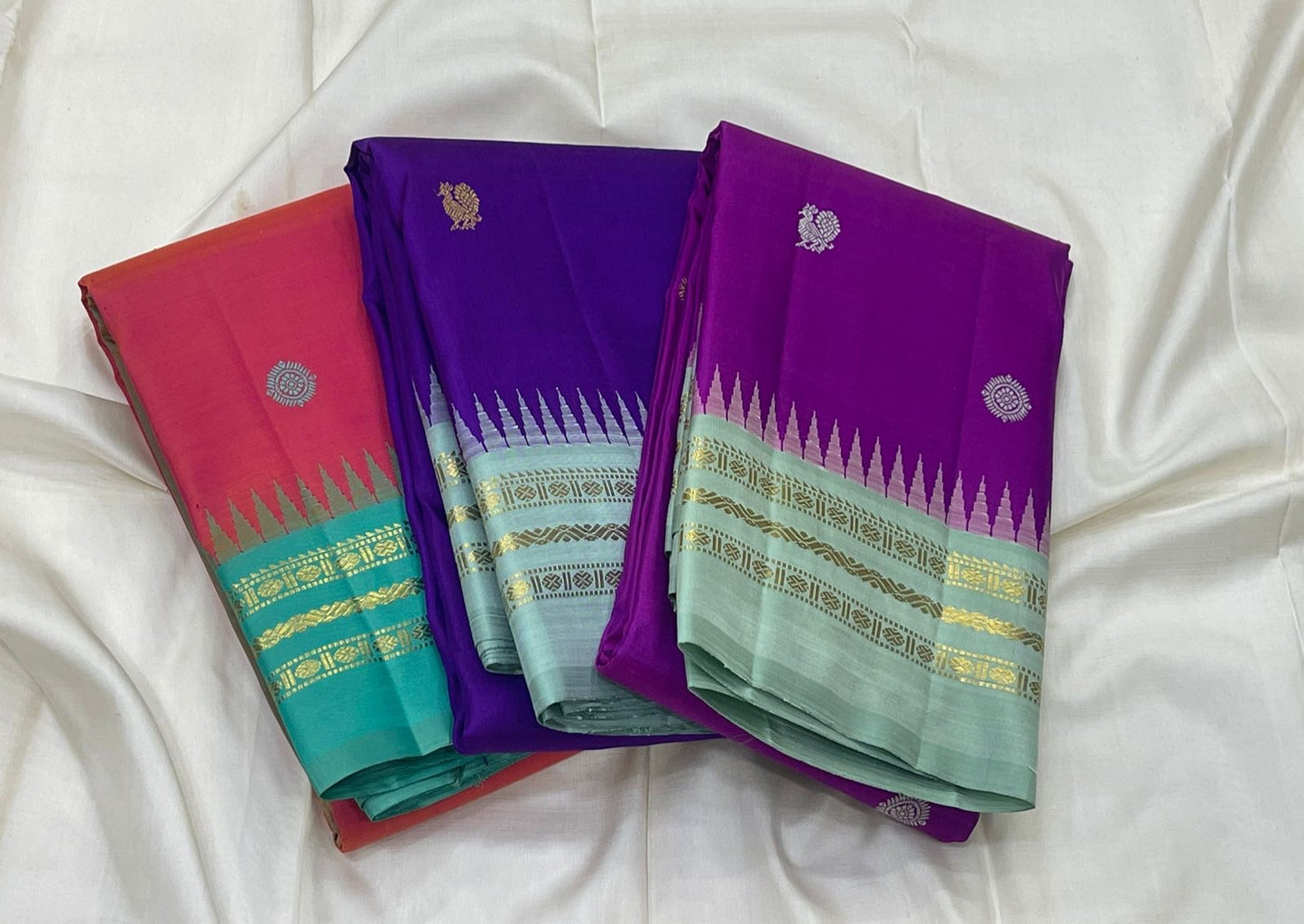 Shot colour tomato red pink and teal Kancheepuram silk saree folded showing Mayil Chakram body and teal Korvai border