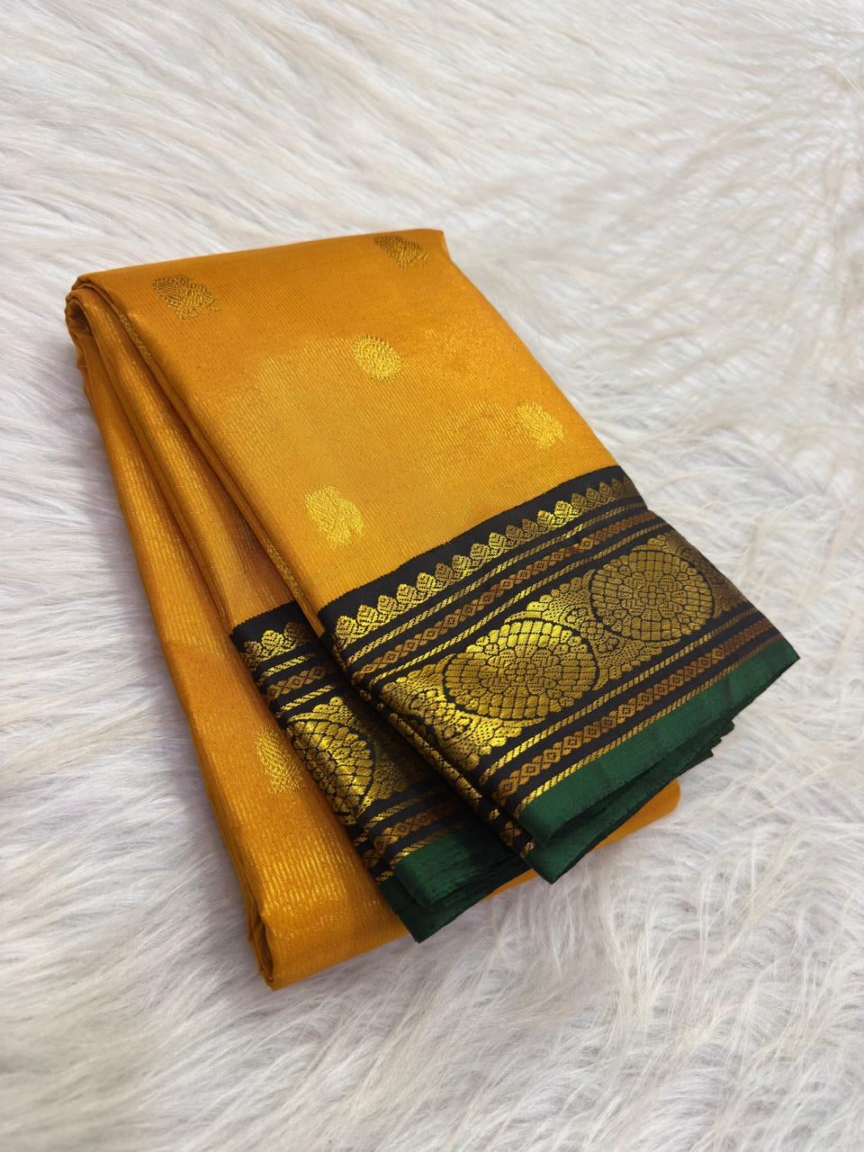 Turmeric yellow Kanchi Pattu with vertical Vairaoosi lines, gold buttas and black Kai Korvai Kamalam border with green edging.