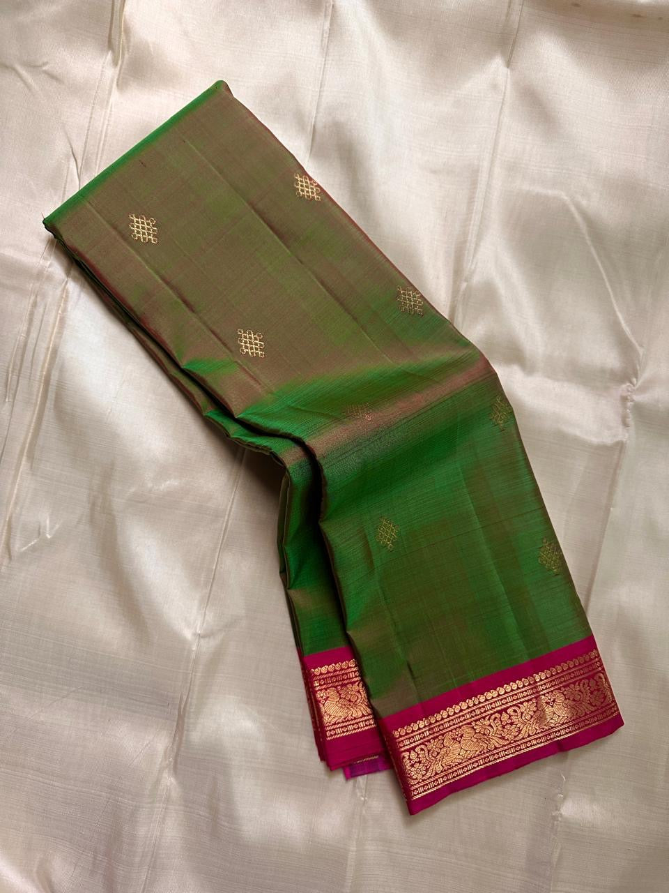 Olive green pure Kanchipuram silk saree shown folded with small gold buttas and a magenta zari woven border.