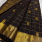 Angled flat lay of black kanchipuram silk saree with gold zari checks and gold border panels