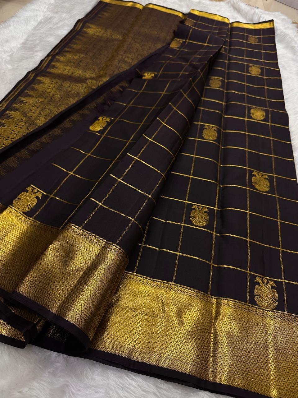 Angled flat lay of black kanchipuram silk saree with gold zari checks and gold border panels