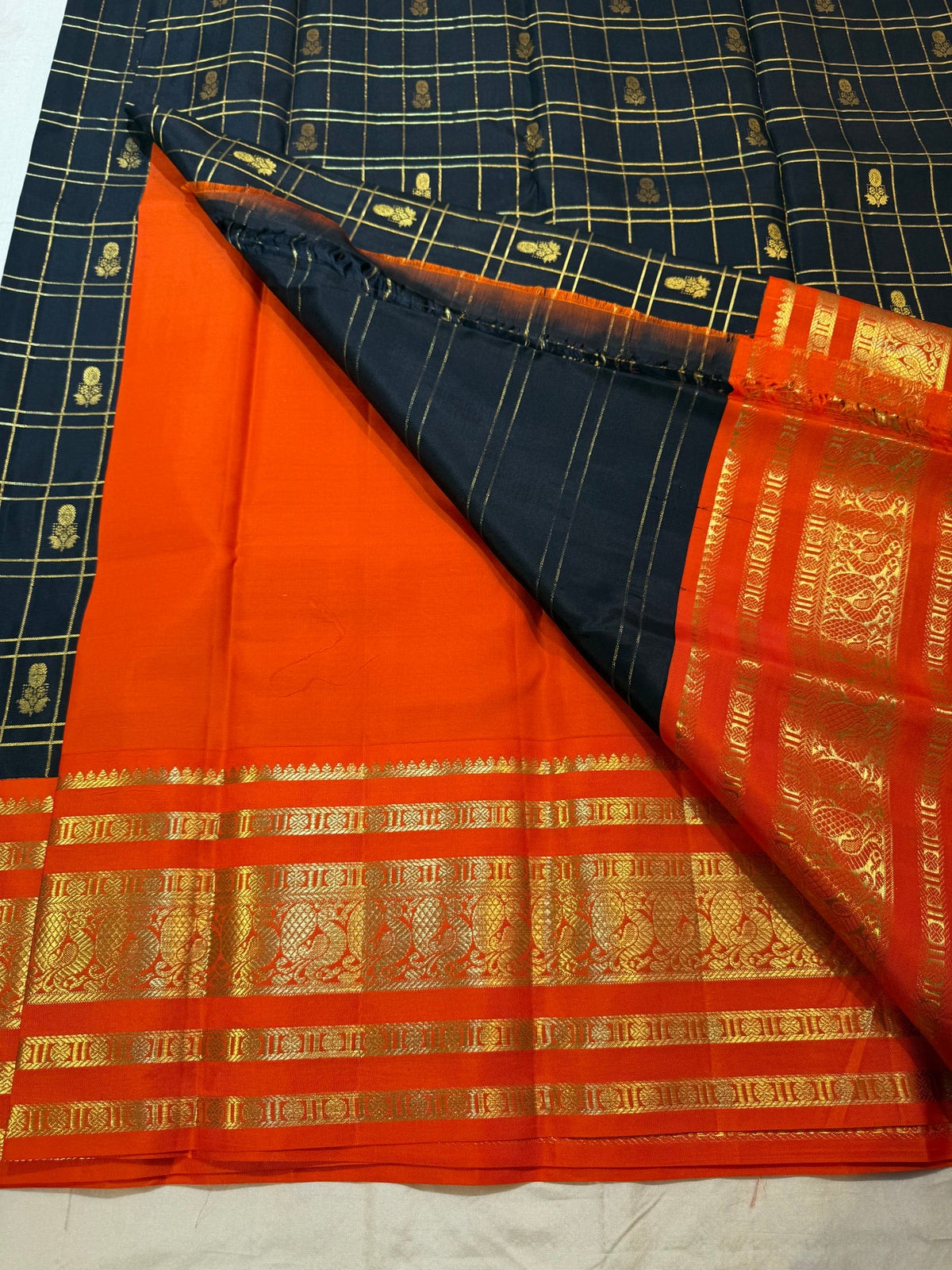 Black Zari Kattam body meeting a saturated burnt-orange border with layered classic-gold zari detailing.