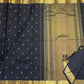 Draped view of midnight black Kanchipuram silk saree highlighting small contrast buttas and wide antique gold zari border with tassels.