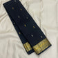 Midnight black Kanchipuram silk saree folded, featuring small contrast buttas across the body and a broad paisley border woven in antique gold zari.