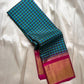 Draped blue-green checked Kanchipuram silk saree showing magenta border and wide gold zari panel on an ivory backdrop