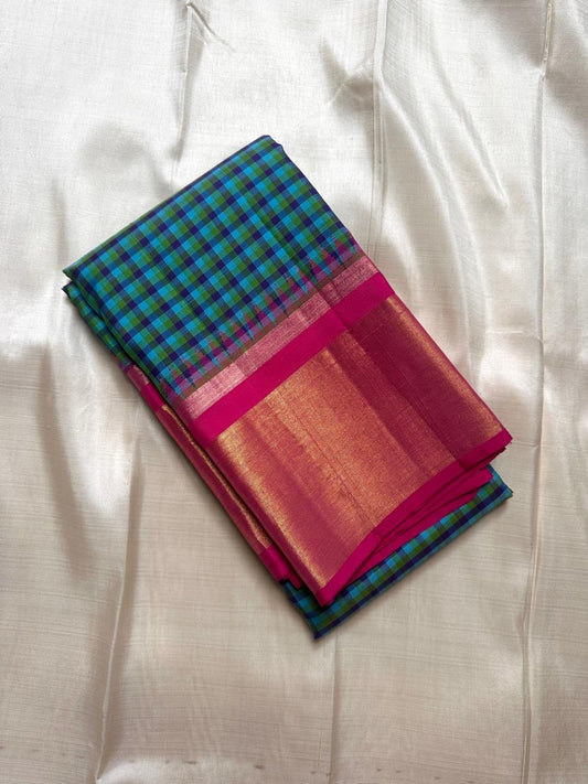 Folded blue-green checked Kanchipuram silk saree with magenta border and gold zari section on an ivory backdrop