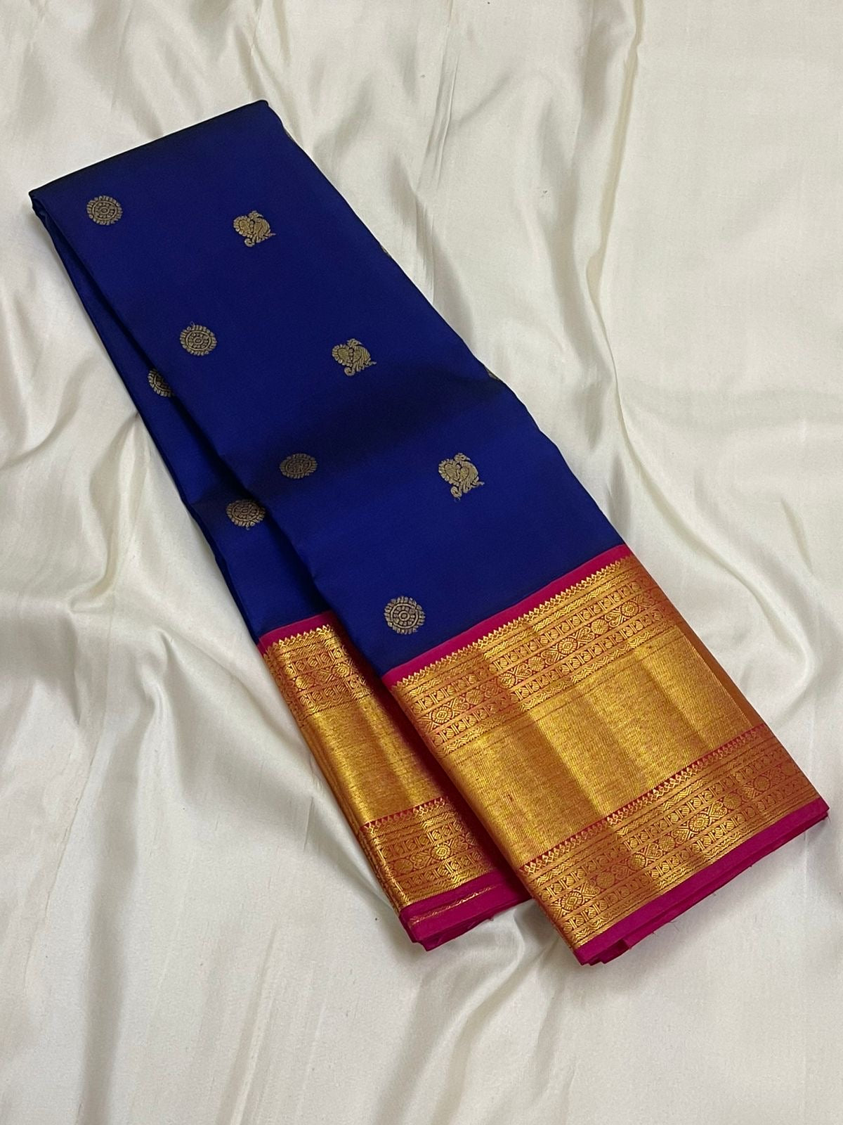 Blue Kanchipuram silk saree folded lengthwise with small gold zari buttas and a wide gold zari border with pink edge.