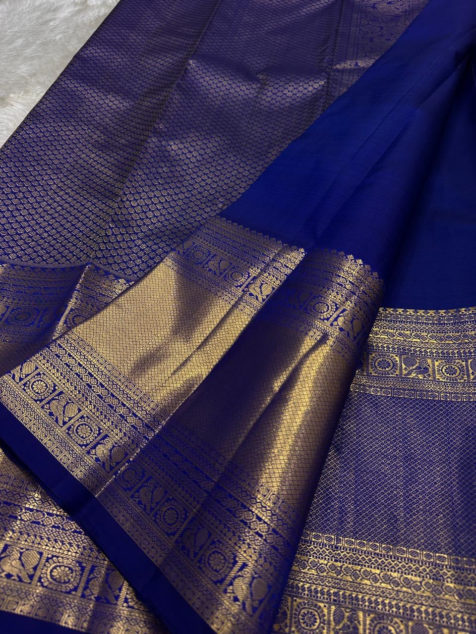 Royal blue saree showing small gold buttas and gold zari border, draped on light fabric, available in the USA
