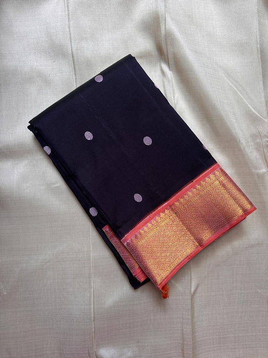 Deep night blue Kanchipuram silk saree with peach border and antique gold zari detailing, neatly folded against a neutral backdrop