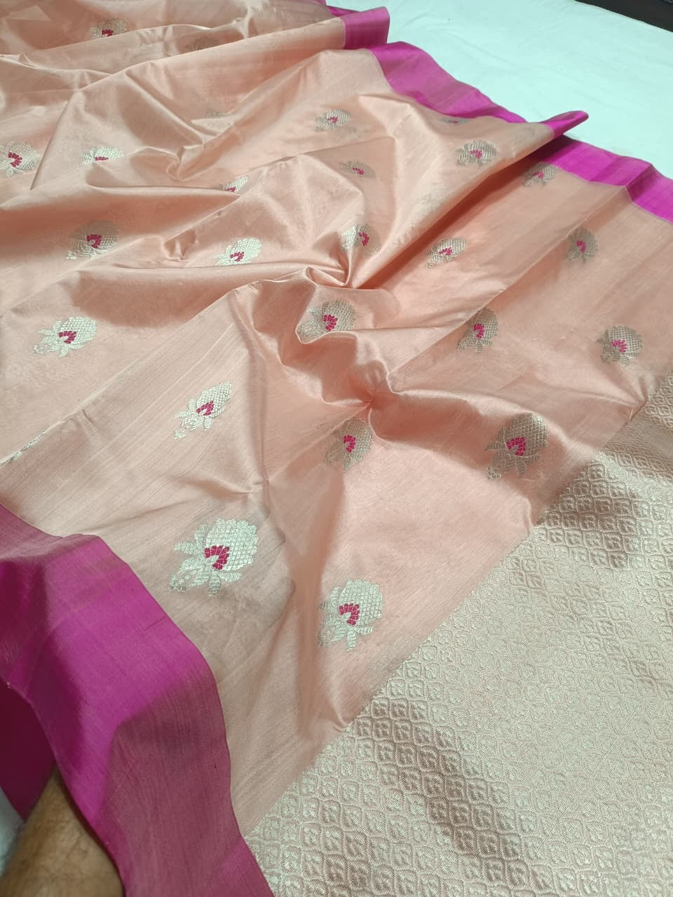 Blush Peach Pattu Silk Chanderi saree folded to show silver floral buttas with Rani Pink accents and contrast edge